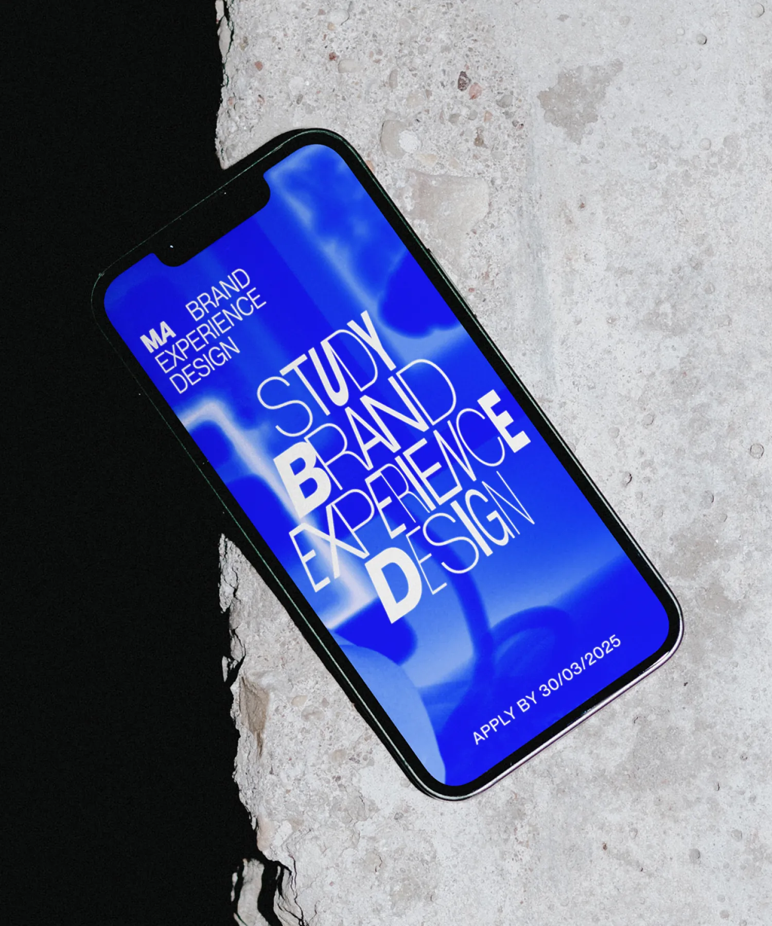 Smartphone on stone surface displaying blue MA Brand Experience Design recruitment graphic