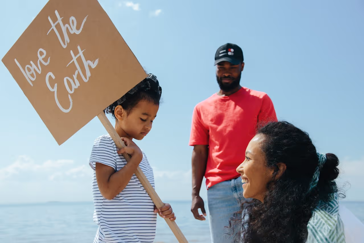 A child holding a sign that reads 'Love the Earth' stands beside two adults.