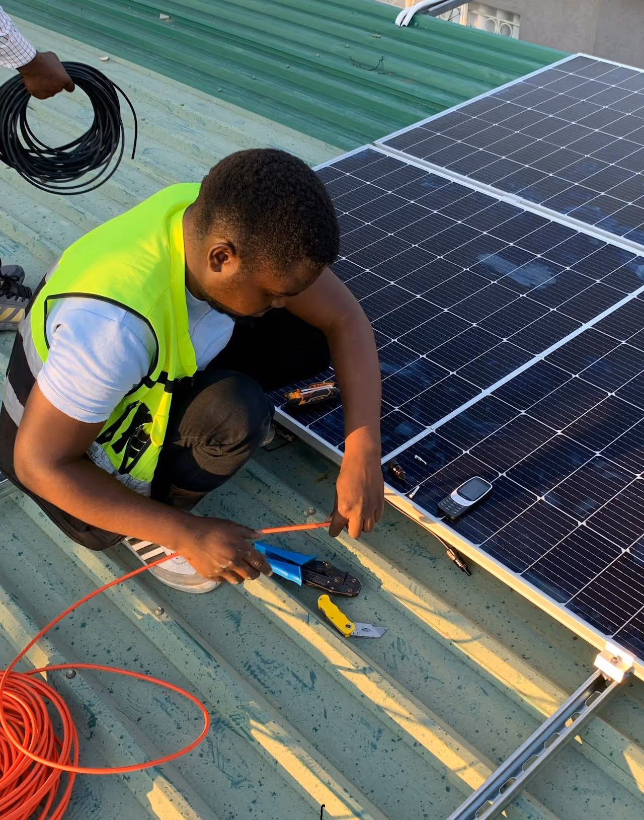 A person in a high-visibility vest installs solar panels on a green metal roof.