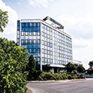 Современное многоэтажное стеклянное офисное здание, окруженное деревьями и асфальтированной дорогой.