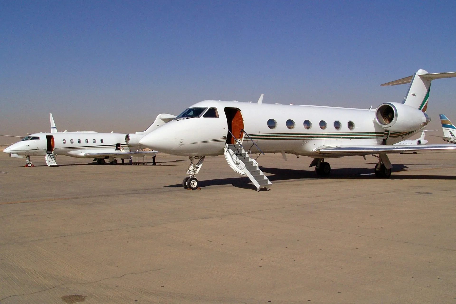 Two white private jets parked on a desert runway under a clear blue sky with open passenger doors and stairs.