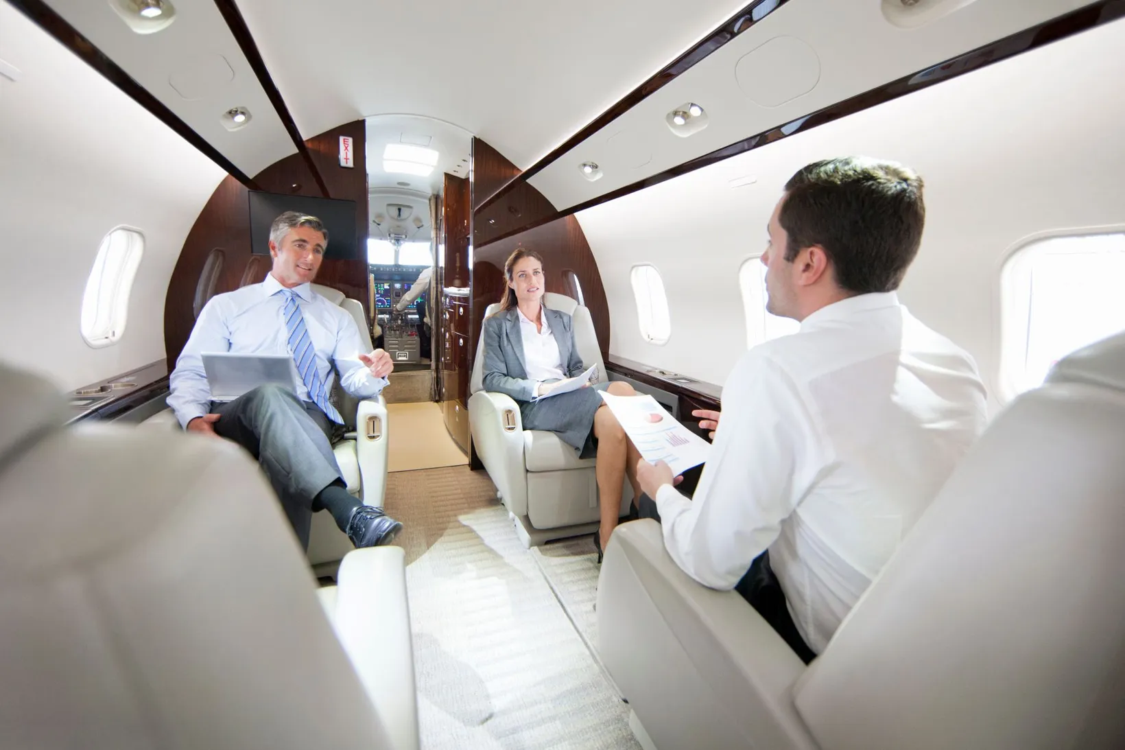 Three business professionals having a meeting inside a private jet, two seated facing a man holding charts.