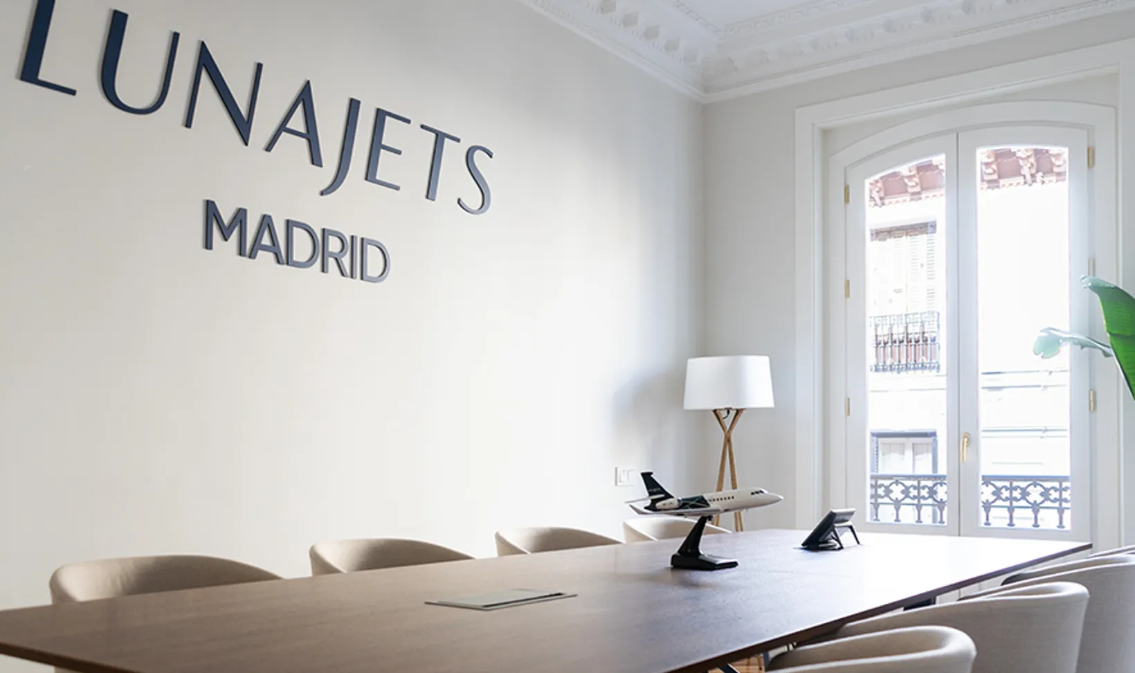 Modern office conference room with LUNAJETS MADRID sign on wall, wooden table, chairs, and model airplane.