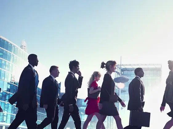 Profesionales de negocios que caminan a paso ligero frente a modernos edificios de oficinas de vidrio durante el día.