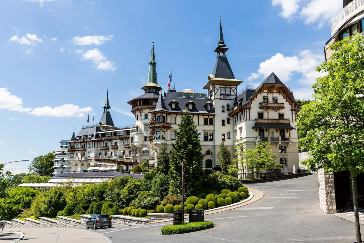 Historic grand hotel with multiple pointed towers surrounded by greenery under a blue sky.