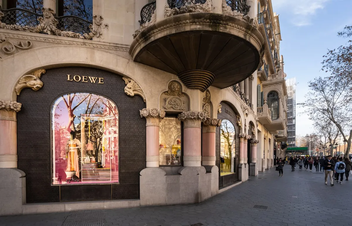 Facade of Loewe store with ornate stone architecture and large display windows on a busy city street.