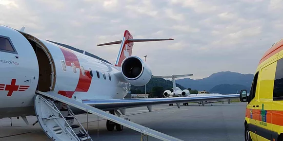 Aereo medico con porta e scale aperte accanto a un'ambulanza sulla pista di un aeroporto.