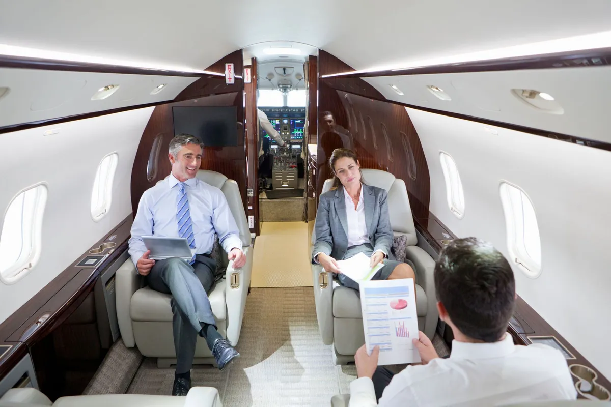 Three business professionals seated inside a private jet cabin, reviewing documents during a meeting.