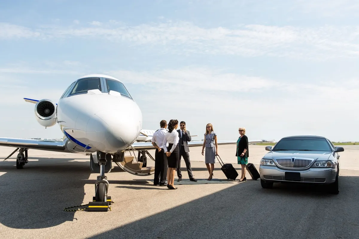 Group of business people standing by a private jet on the tarmac with luggage and a silver limousine nearby.