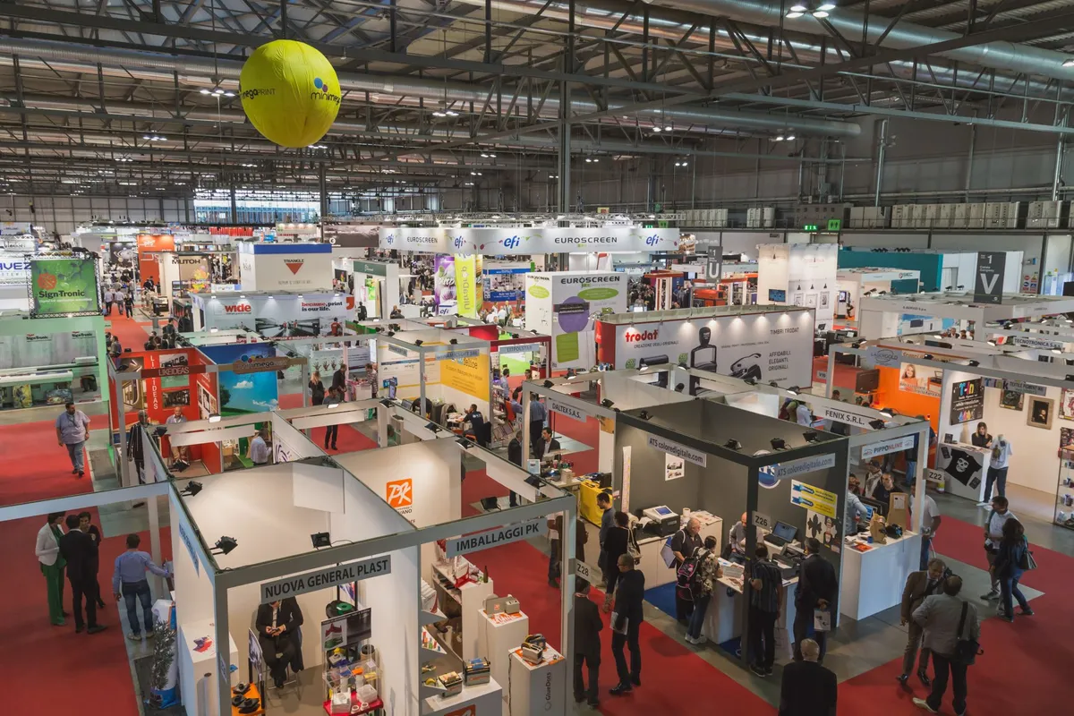 A large exhibition hall filled with booths and attendees at a trade show, featuring brands like Euroscreen and Trodat.