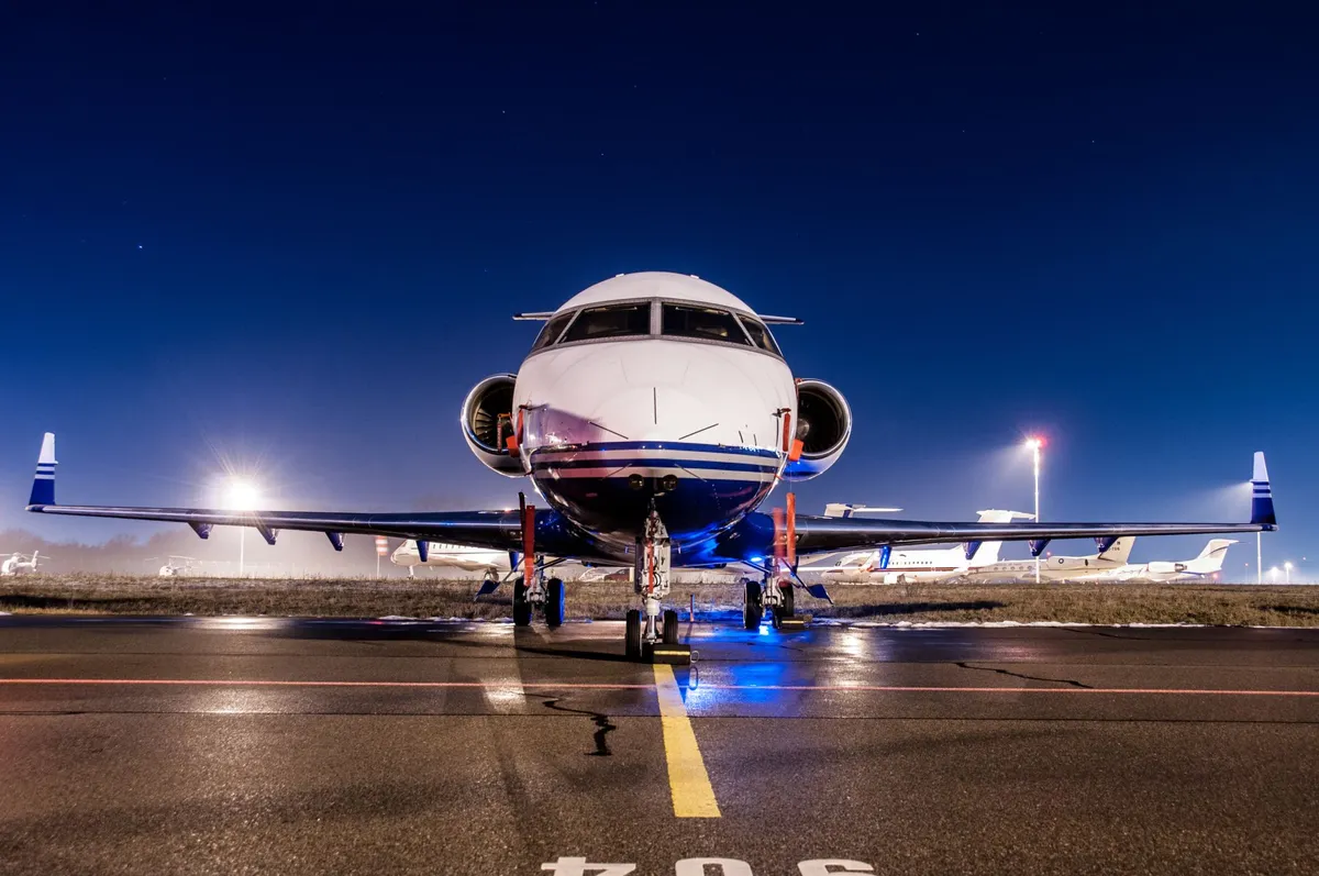 Front view of a private jet parked on an airport tarmac at night under a clear starry sky.