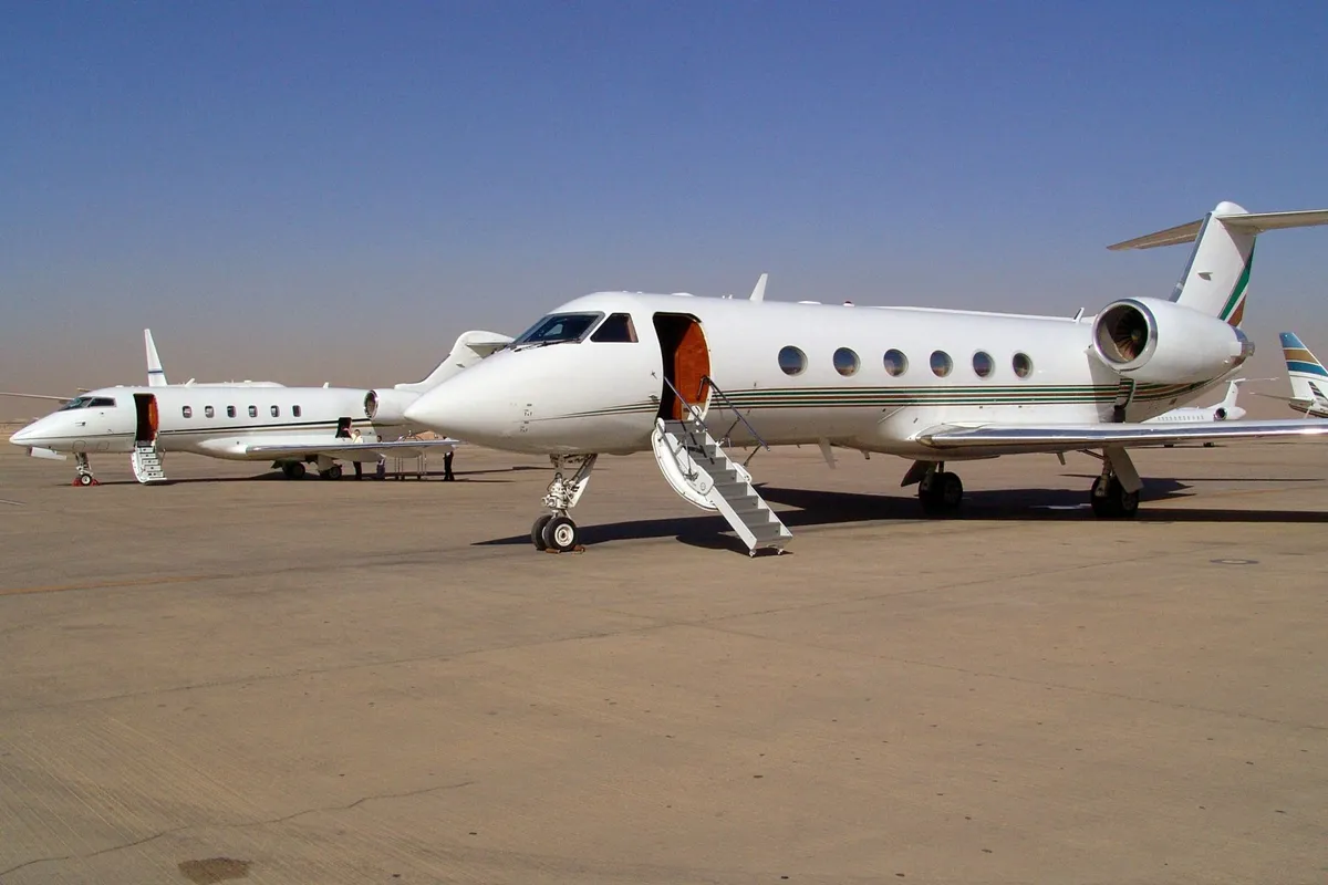 Two white private jets parked on a runway with their boarding stairs extended under a clear blue sky.