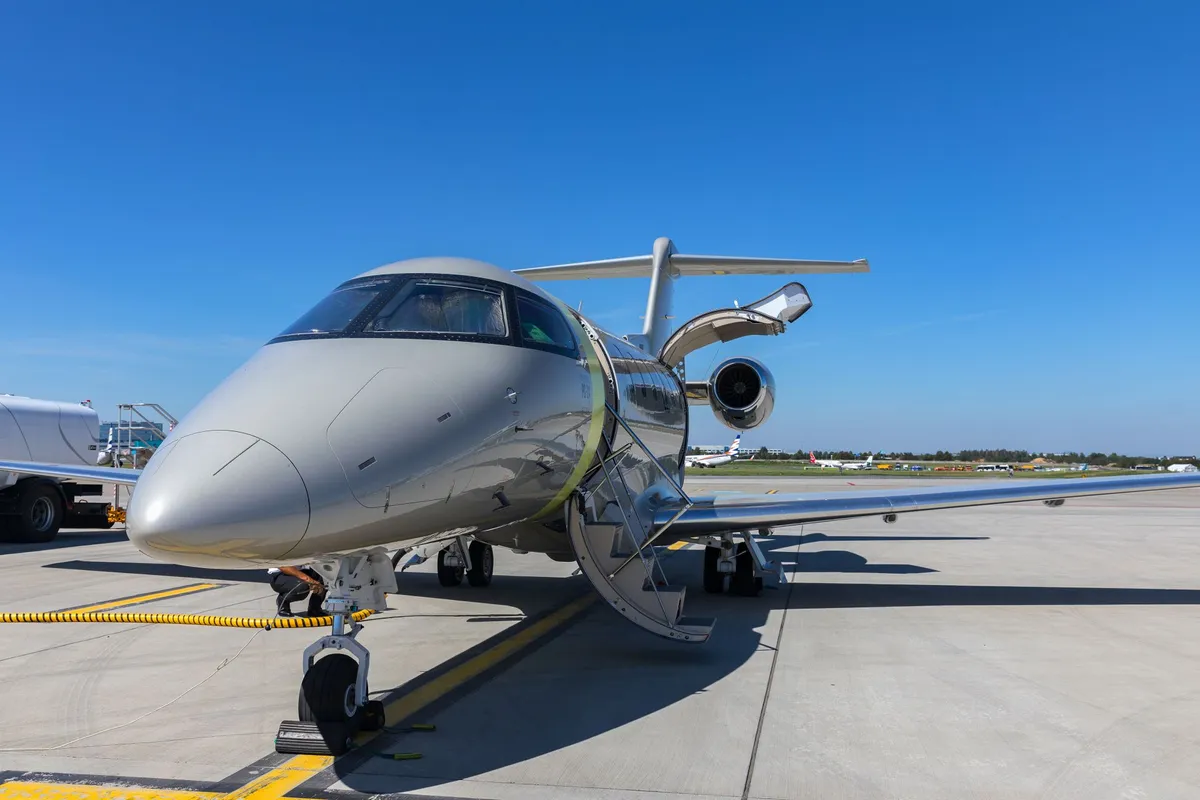 Gray Pilatus PC-24 jet with open door and staircase parked on airport tarmac under clear blue sky.