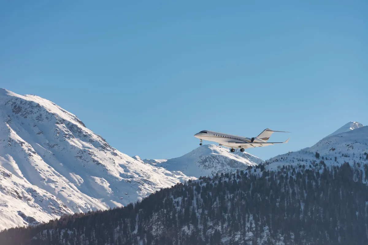 Private jet flying low over snow-covered mountains with a clear blue sky.