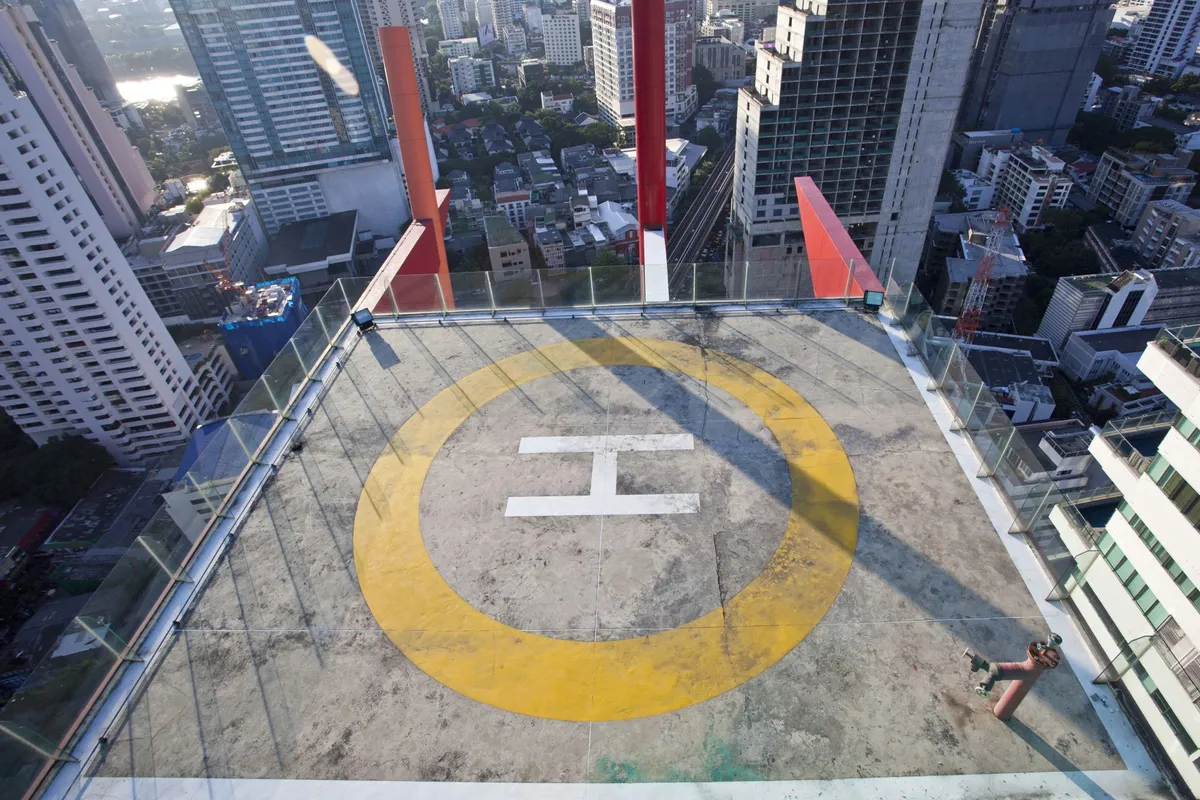 Helipad with yellow circle and white H on rooftop surrounded by glass barriers on a city building.