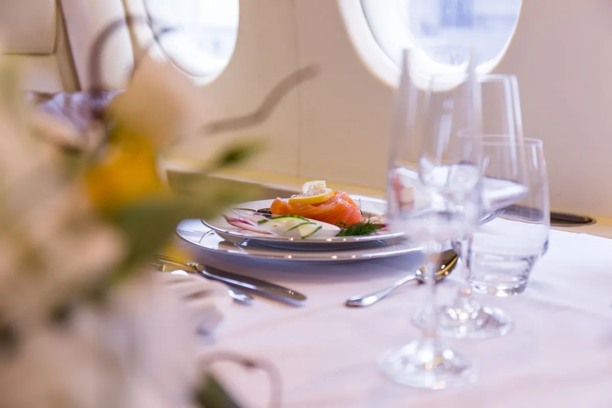 Gourmet appetizer with smoked salmon, lemon, and vegetables on a plate set on a white tablecloth inside a private jet cabin.