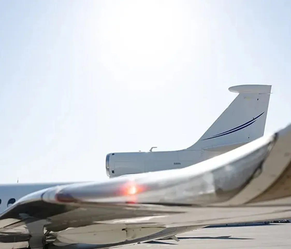 Vista ravvicinata dell'ala e della coda di un jet privato su un asfalto soleggiato.