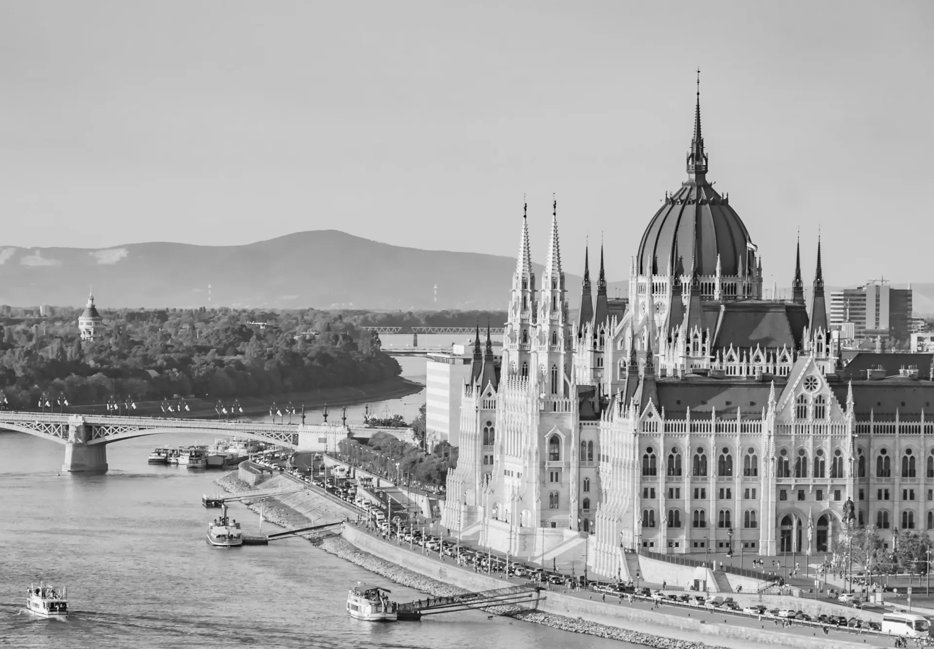 Photo en noir et blanc du bâtiment du Parlement hongrois le long du Danube avec des bateaux et un pont en arrière-plan.