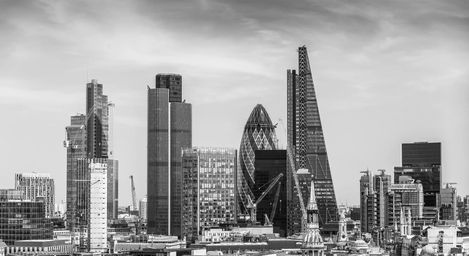 Black and white image of London skyline featuring The Gherkin and The Shard skyscrapers with construction cranes visible.