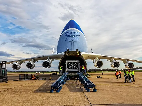 Front view of a large cargo plane with its nose open and ground crew loading freight using conveyor belts.