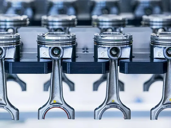 row of shiny metallic engine pistons with connecting rods, likely part of a high-performance engine assembly