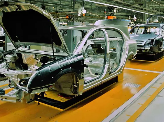 Car frames on an assembly line in a factory with open doors and hoods.