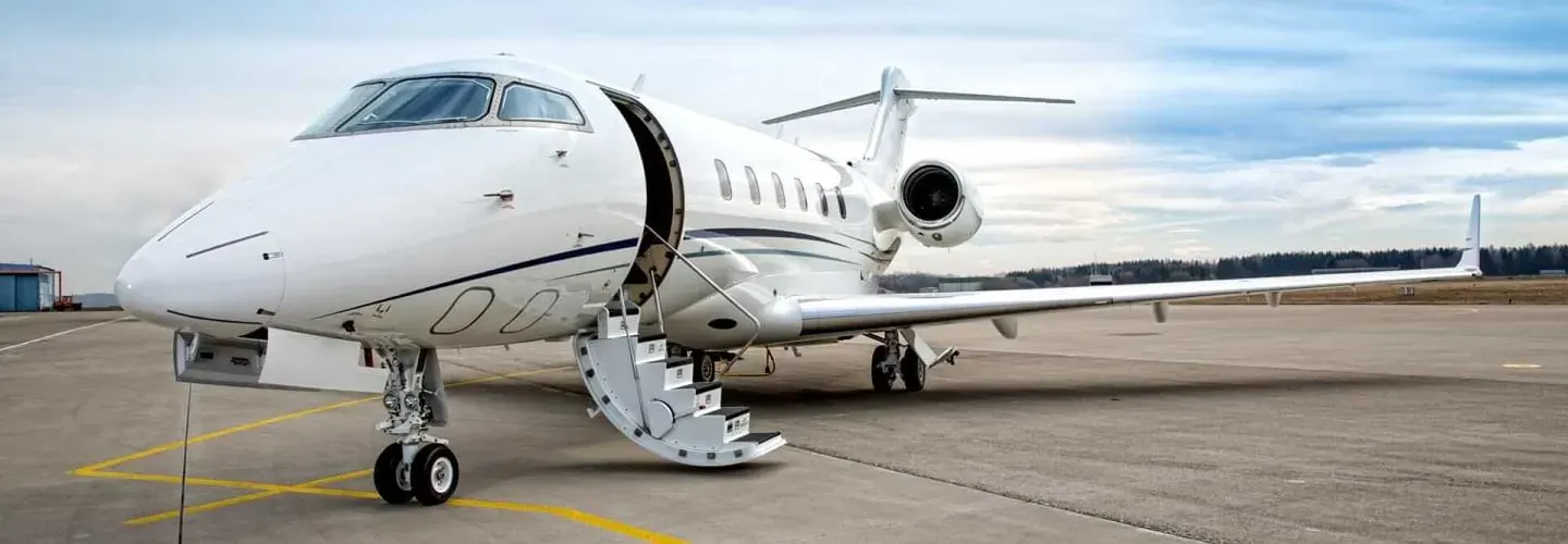 White private jet with open door and stairs on a runway under a cloudy sky.
