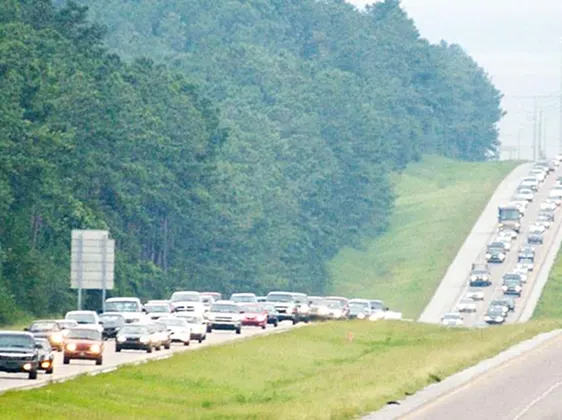 Two-lane highway with dense traffic jam and forested area on the left side.