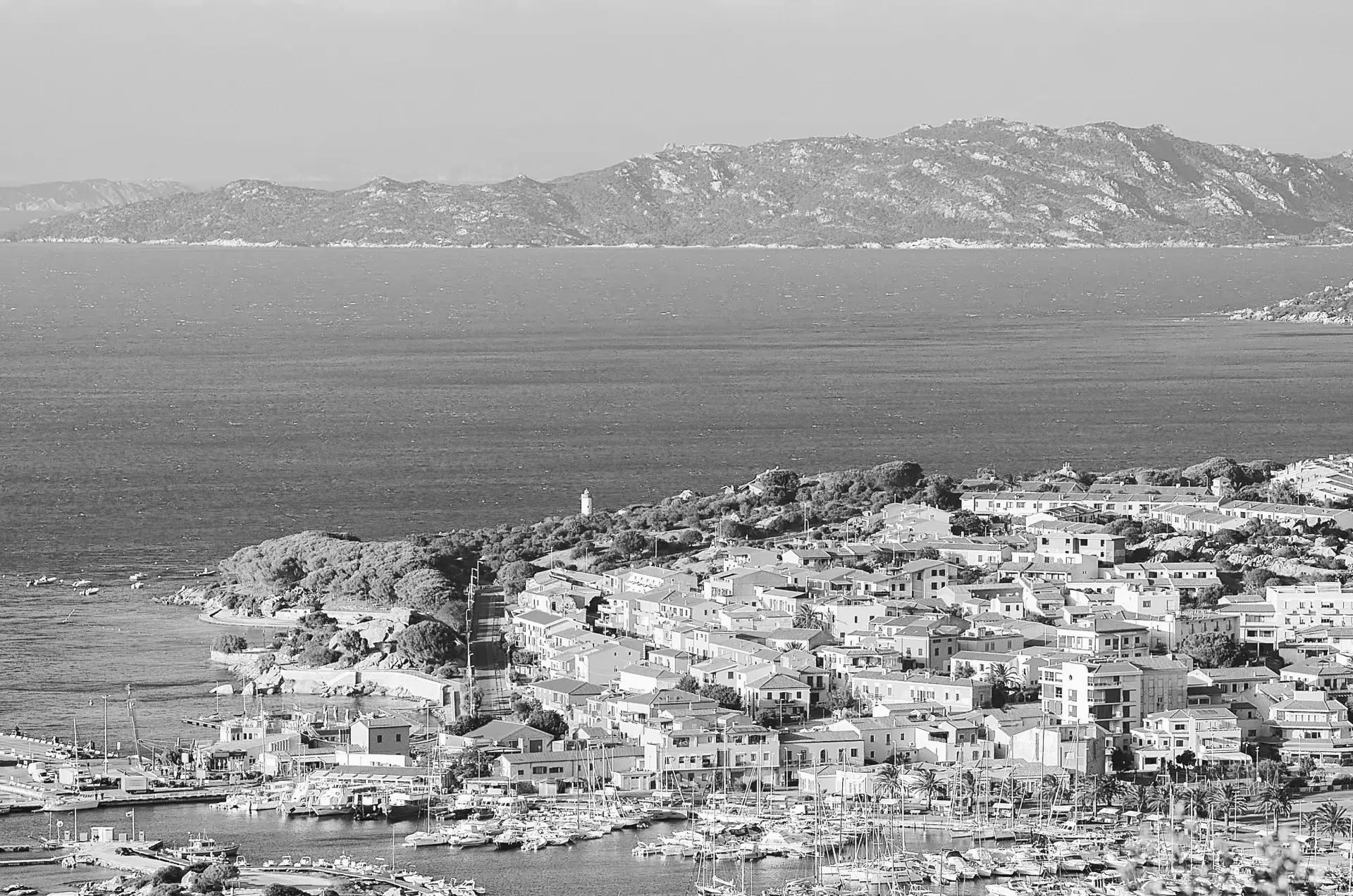 Olbia with a marina filled with boats, clustered buildings, a lighthouse, and mountainous terrain across the water.
