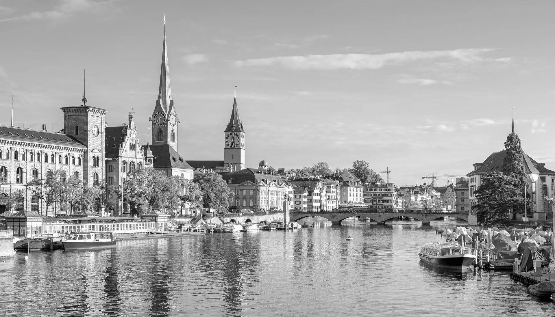 View of Zurich city skyline featuring historic buildings, church steeples, and boats docked along the river.