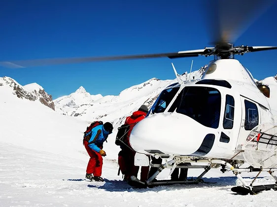 White helicopter with skiers on snowy mountain landing zone for luxury ski resort transfer
