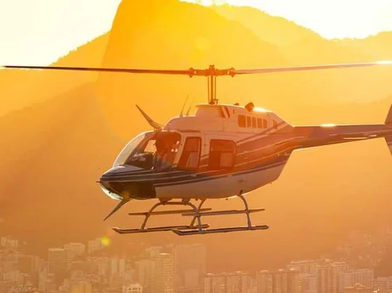 Helicopter silhouette flying over city at golden sunset for panoramic sightseeing tour
