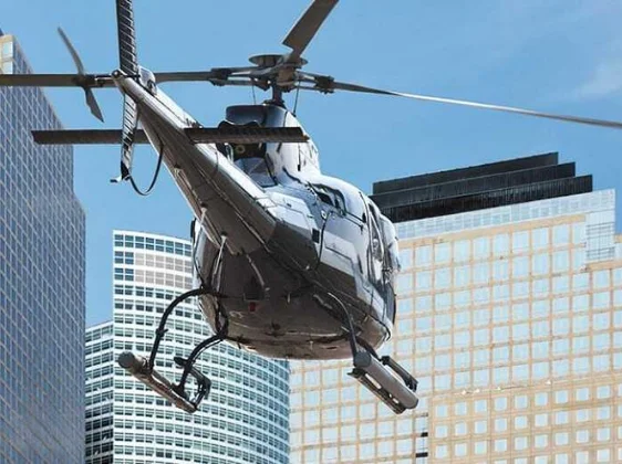 Silver helicopter flying between modern skyscrapers for VIP city airport transfer service