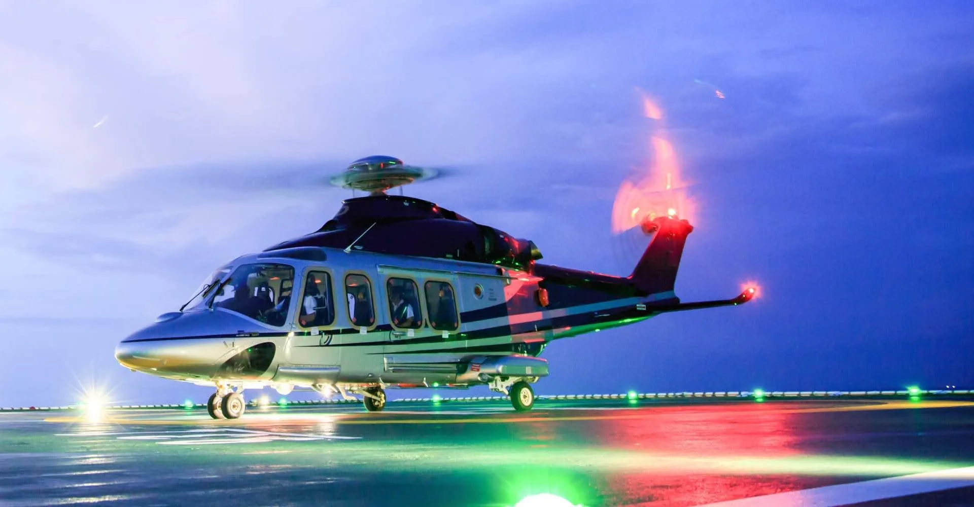 Modern luxury helicopter with green and yellow livery on illuminated helipad at twilight for private VIP charter and transfers