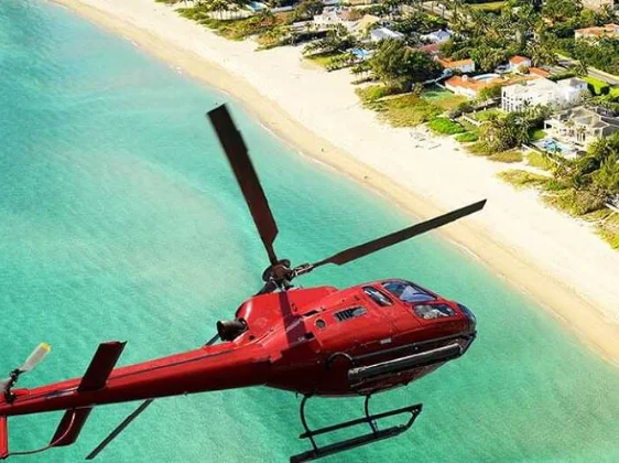 Red helicopter flying over turquoise ocean and pristine beach for remote island charter access