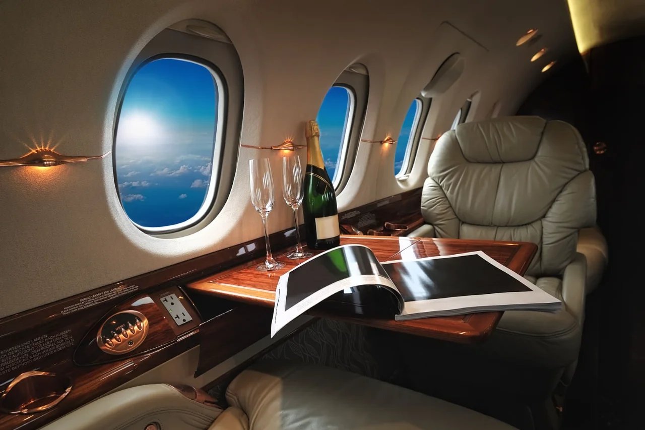 Luxurious private jet cabin interior with leather seats, champagne glasses, and windows showing blue sky