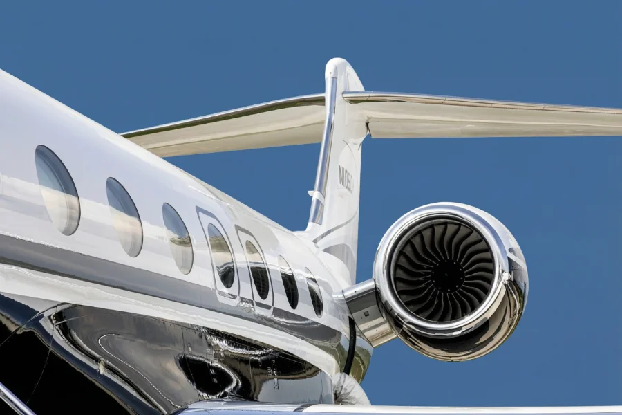 Nahaufnahme des Heckbereichs eines Privatjets mit Fenstern, Heck und Triebwerksturbine vor einem strahlend blauen Himmel.