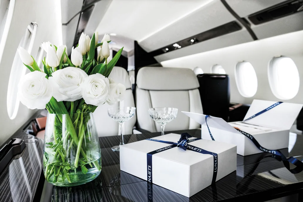 Luxuriöse Innenausstattung für Privatjets mit cremefarbenen Ledersitzen, einem beigen Sofa, Holztischen und Frühstück, das auf einem Tablett serviert wird.