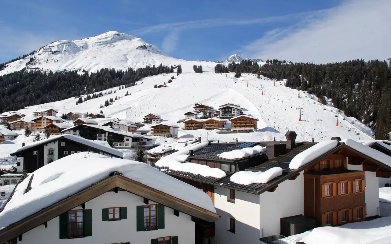 Заснеженные дома в Лех-Цюрсе с лыжными склонами под чистым голубым небом.