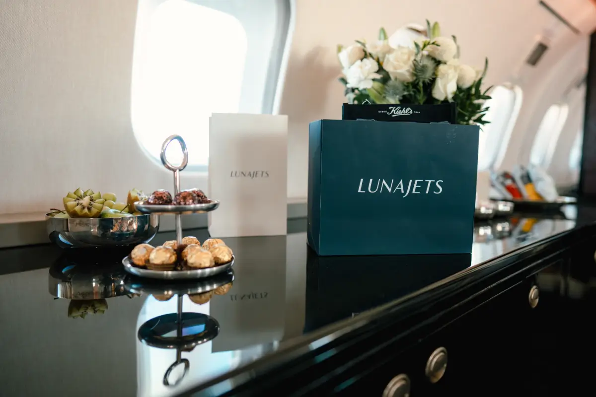 LunaJets márkájú táska és catering tányér gyümölccsel és süteményekkel egy magánrepülőgép kabinjában