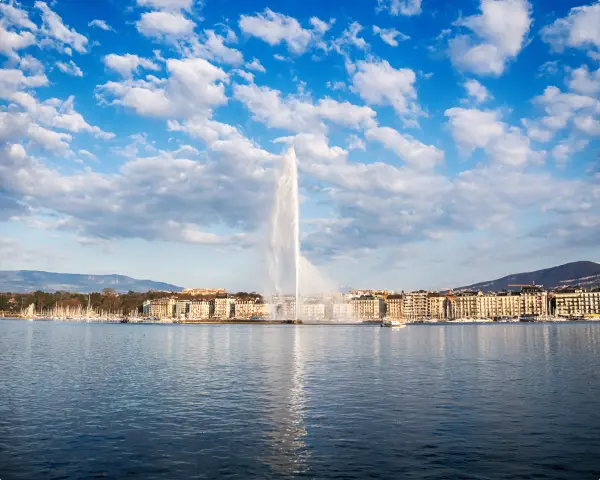 Genfersee mit einer großen Wasserfontäne und zahlreichen Booten im Yachthafen.