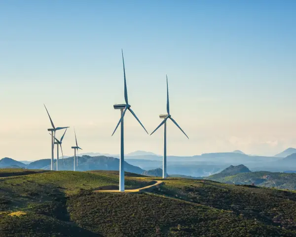 Windkraftanlagen auf grünen Hügeln mit Bergen im Hintergrund