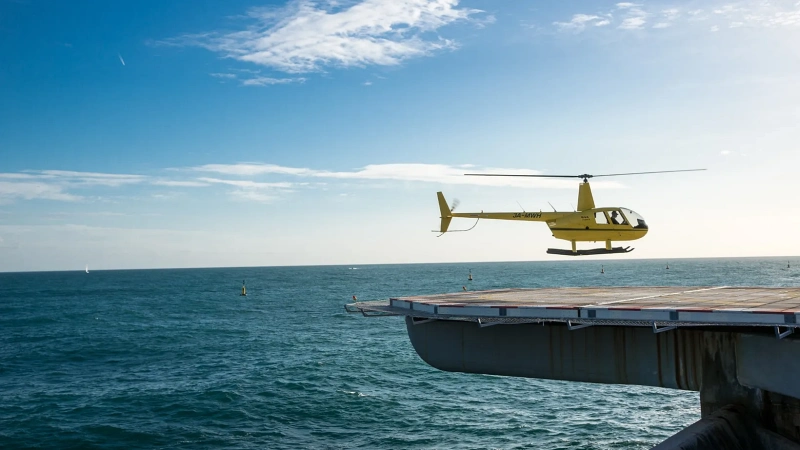 Żółty helikopter zbliżający się do Heliport Monako nad Morzem Śródziemnym, oferujący malownicze transfery z pobliskich lotnisk.