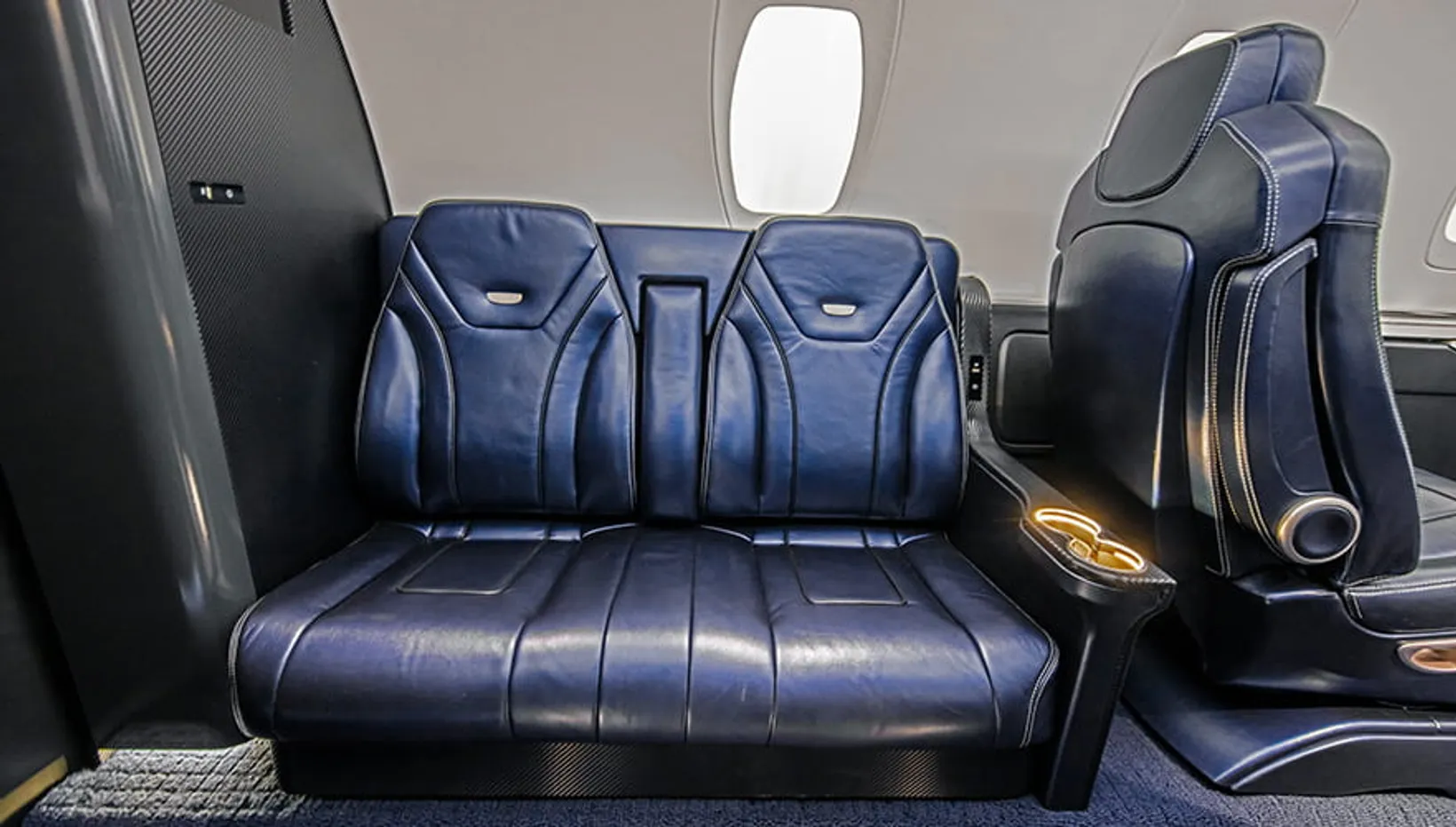 Cessna Citation XLS cabin interior showing luxury blue leather seats, window, and overhead compartments in parked aircraft.