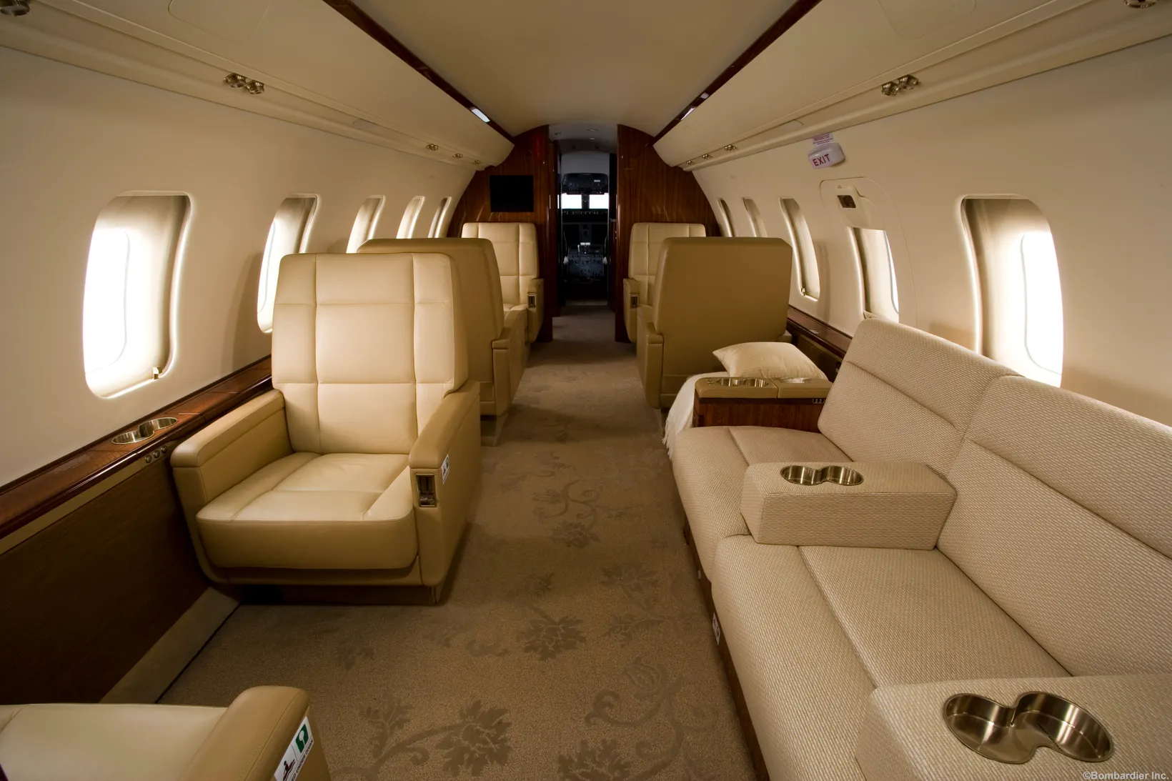 Bombardier Challenger 604 cabin interior featuring cream leather seats, wood paneling, illuminated windows, and carpeted a...