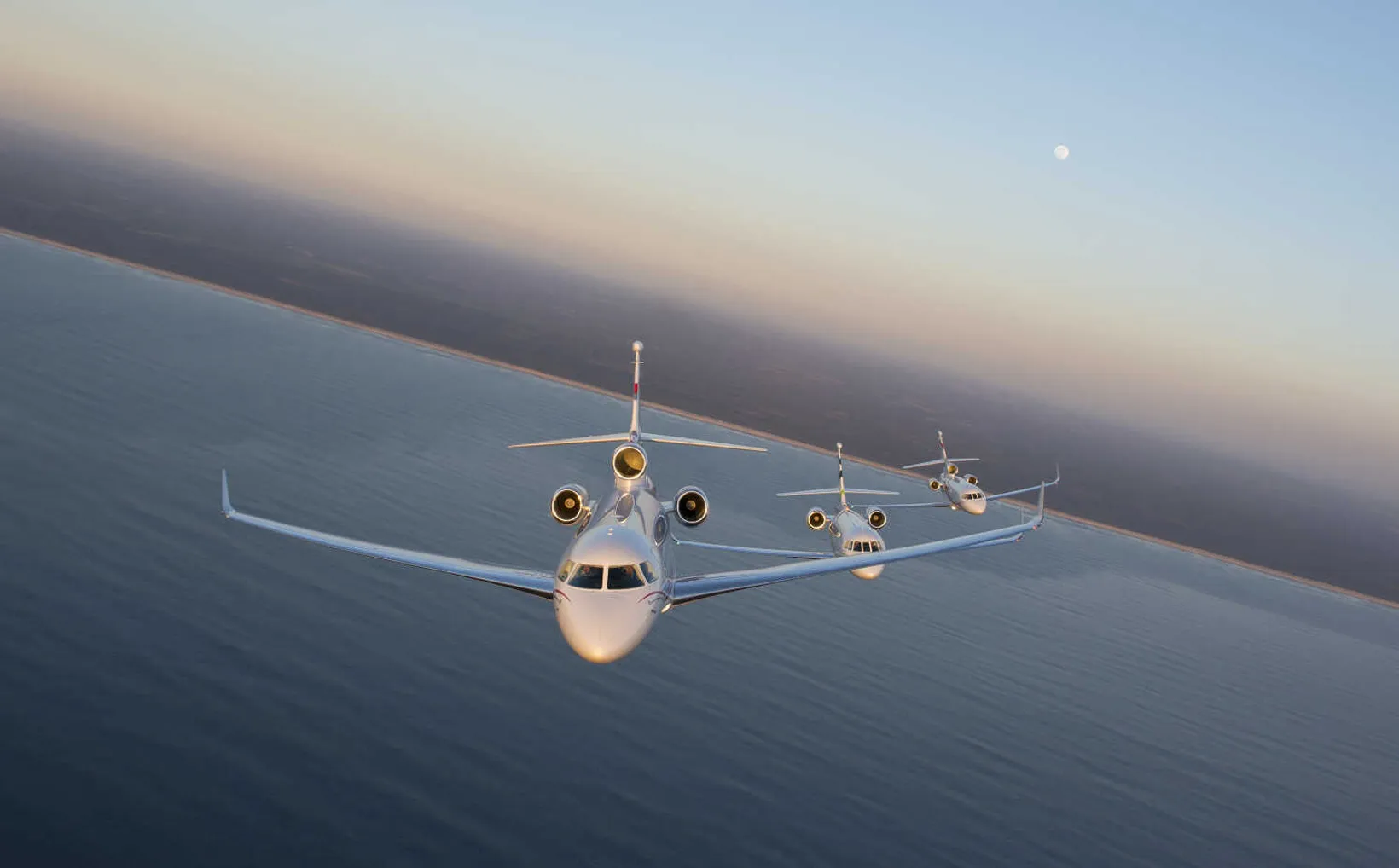 Dassault Falcon 7X in formation flight over ocean at sunrise, three-engine business jet in profile view with golden light ...