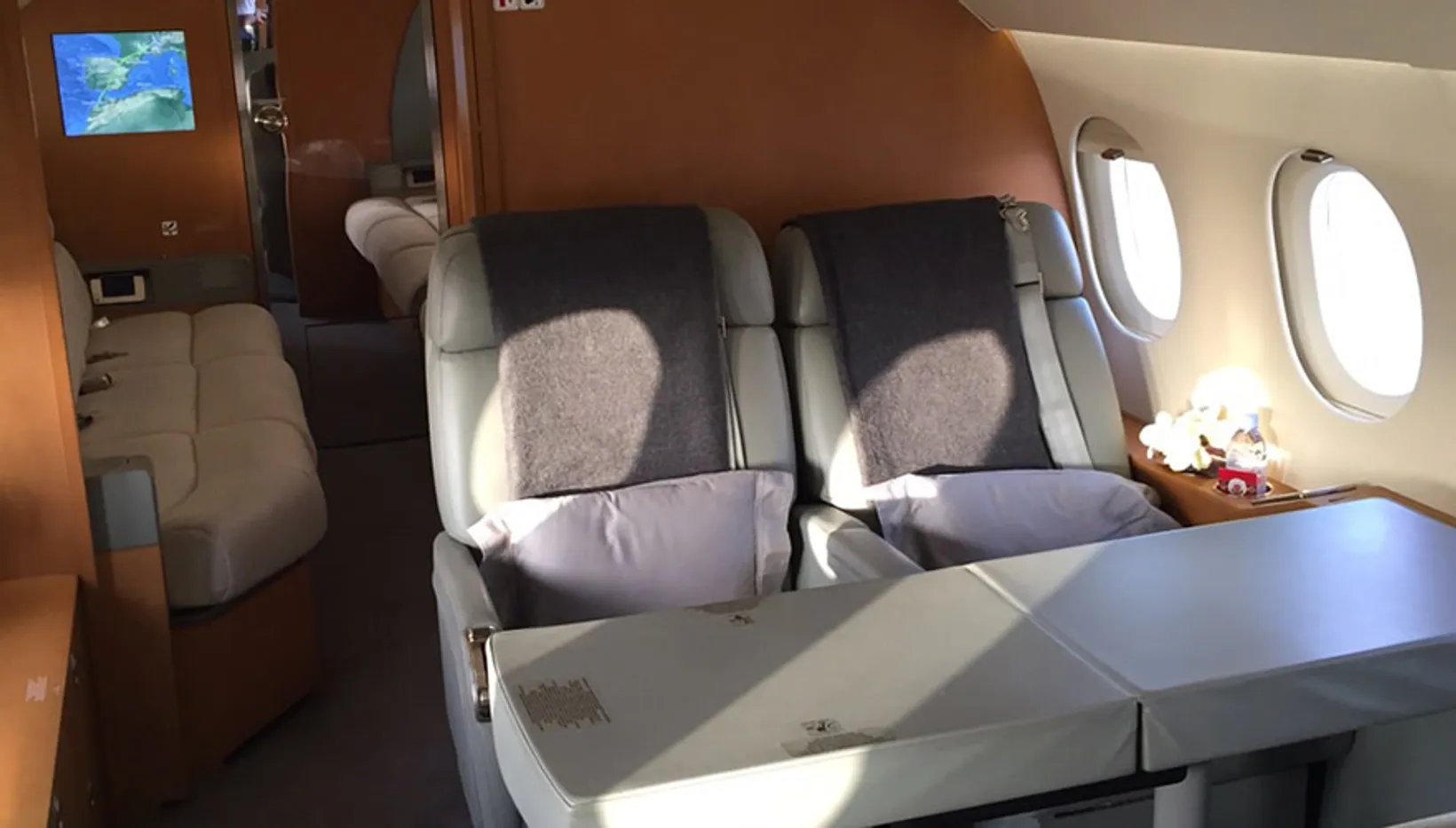 Interior cabin view of Dassault Falcon 900B showing two leather seats with pillows, windows, wooden accents, and entertain...