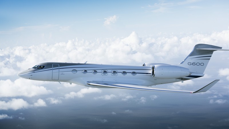 Gulfstream G600 private jet in flight over clouds, side profile view showing sleek silver fuselage and distinctive tail de...
