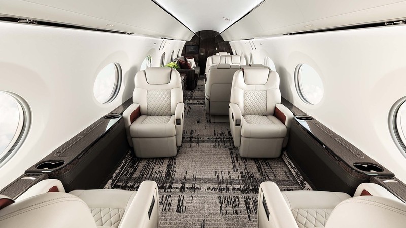 Gulfstream G600 cabin interior featuring cream leather seats, patterned carpet, and round windows along the fuselage.