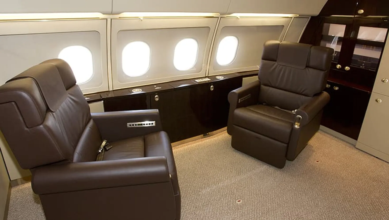 Luxurious cabin interior of Airbus ACJ318 private jet featuring brown leather recliners, oval windows, dark wood paneling,...